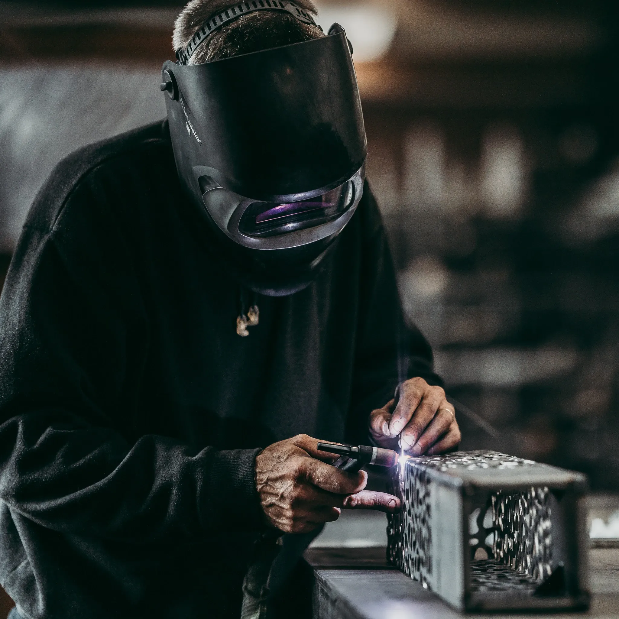 Artisan au travail, masque baissé et lumière ponctuelle.